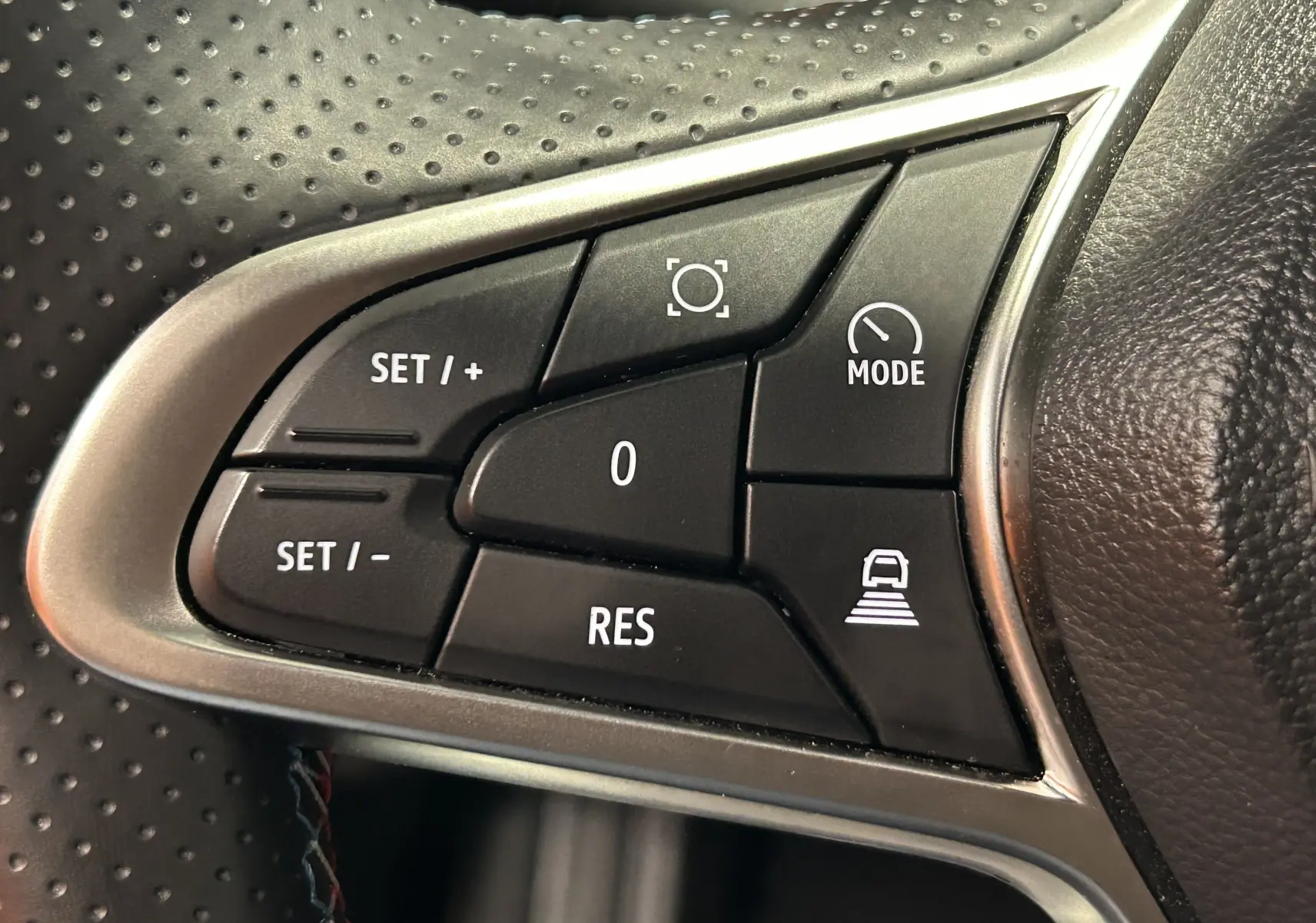 Gros plan sur les commandes de régulateur de vitesse au volant perforé du Renault Captur bleu Iron 2025.