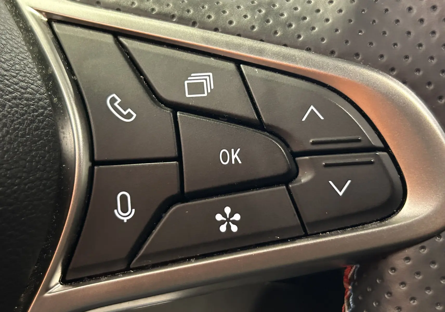 Gros plan sur les commandes multifonctions noires du volant perforé du Renault Captur bleu Iron, version hybride 2025.