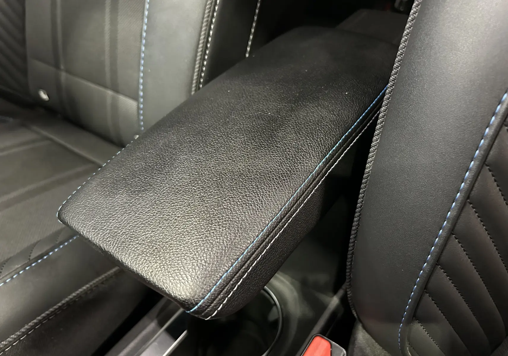 Détail de l'accoudoir central en cuir noir avec surpiqûres bleues sur les sièges avant du Renault Captur II Ph.2.