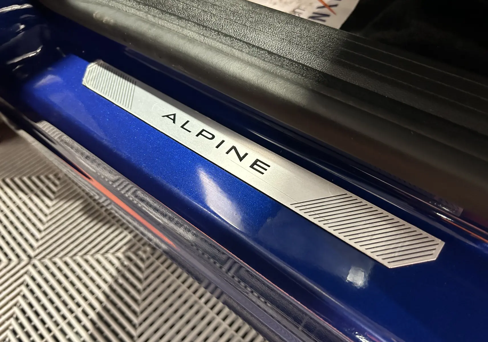 Gros plan sur la plaque de seuil de porte "ALPINE" sur la carrosserie bleu iron du Renault Captur II Ph.2.
