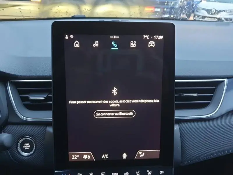 Vue intérieure centrée sur l'écran tactile multifonction du Renault Captur Bleu Iron, avec bouton démarrage visible à gauche.