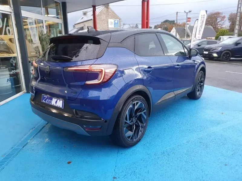 Renault Captur 2025 bleu Iron en vue 3/4 arrière droit, avec jantes alu noires et toit noir contrasté.