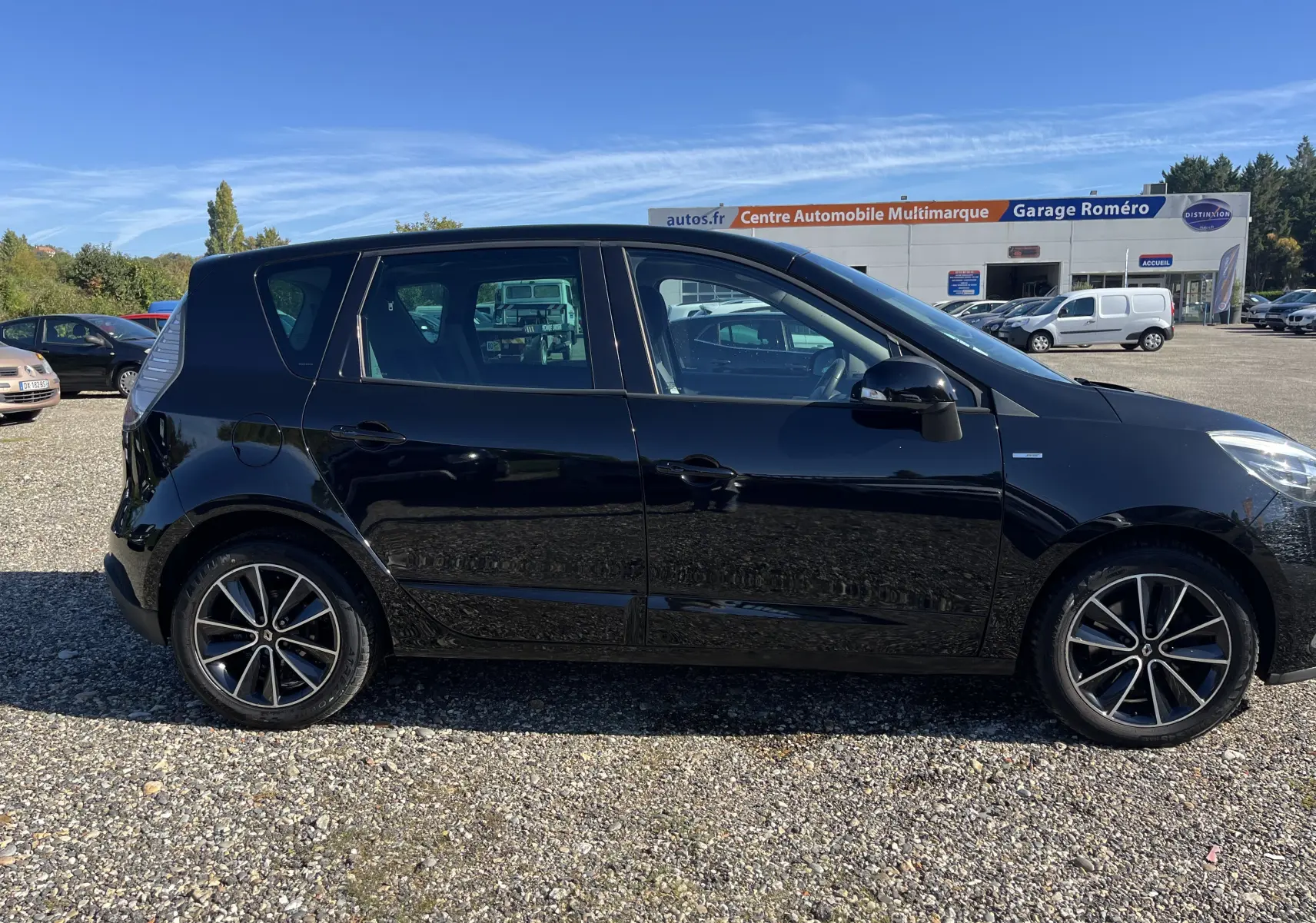 Profil côté gauche d'un Renault Scénic III noir de 2012, avec jantes alliage et vitres teintées, sur parking extérieur.