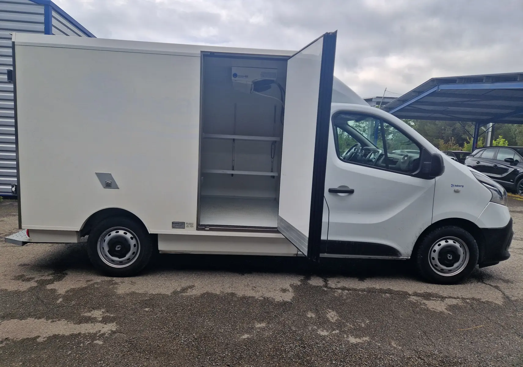 Vue latérale droite d'un Renault Trafic plancher cabine blanc 2019 avec porte latérale ouverte montrant la caisse frigorifique ICEBERG équipée d'étagères.