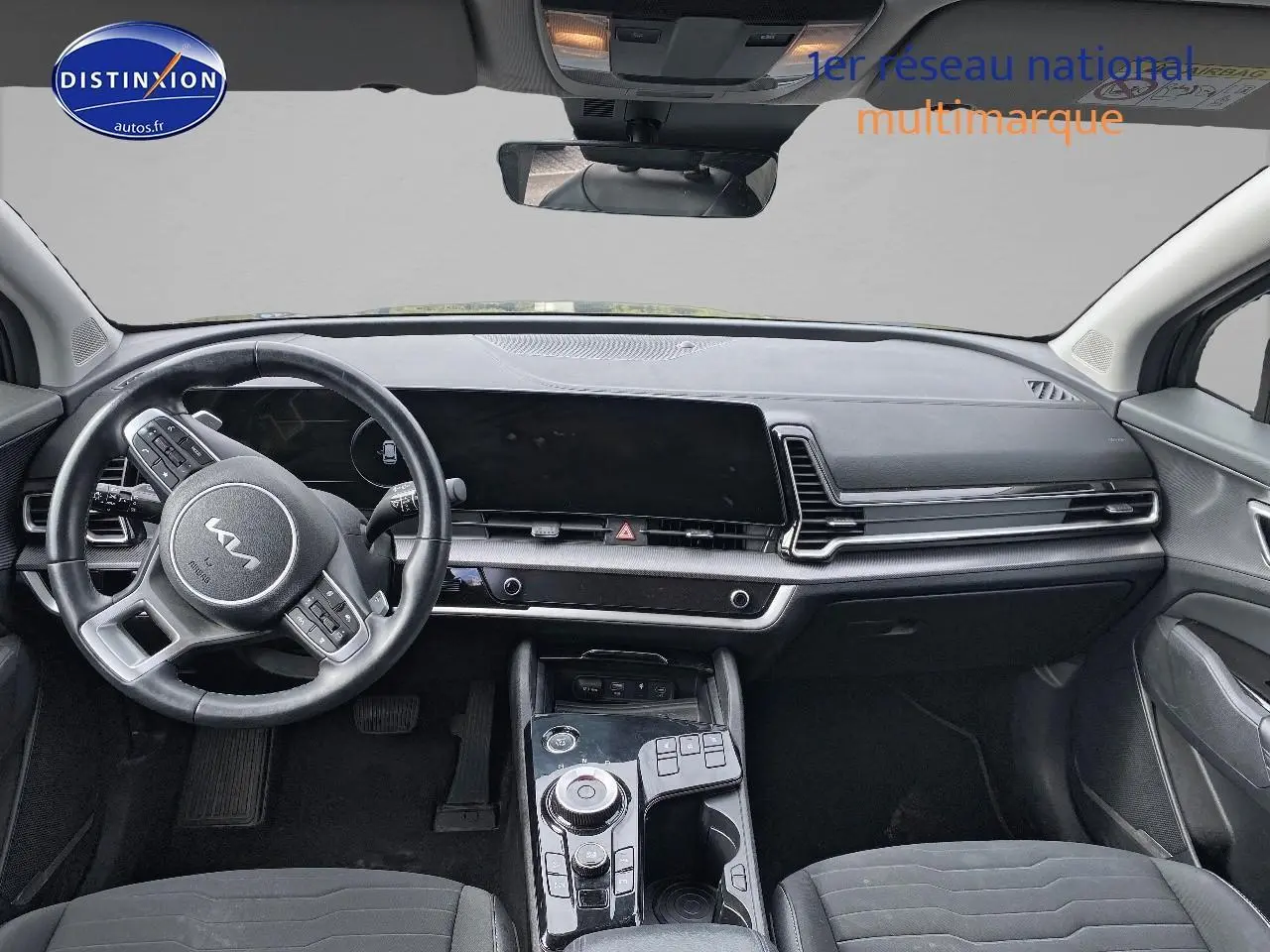 Vue intérieure avant du Kia Sportage 2023 noir, mettant en valeur le tableau de bord moderne et le volant multifonction cuir.