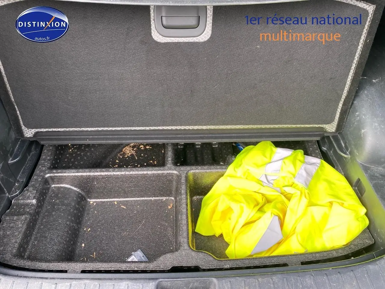 Compartiment de rangement ouvert dans le coffre d'un KIA SPORTAGE noir, avec un gilet jaune visible à droite.