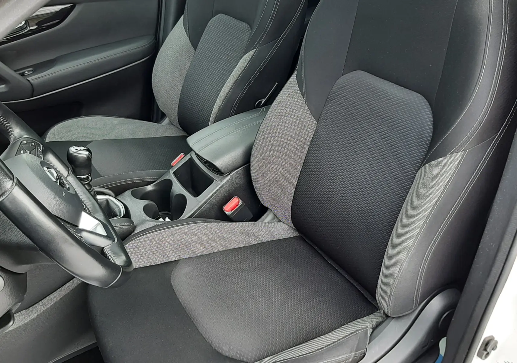Intérieur du Nissan Qashqai blanc 2020, vue rapprochée sur les sièges avant en tissu noir et gris avec console centrale.