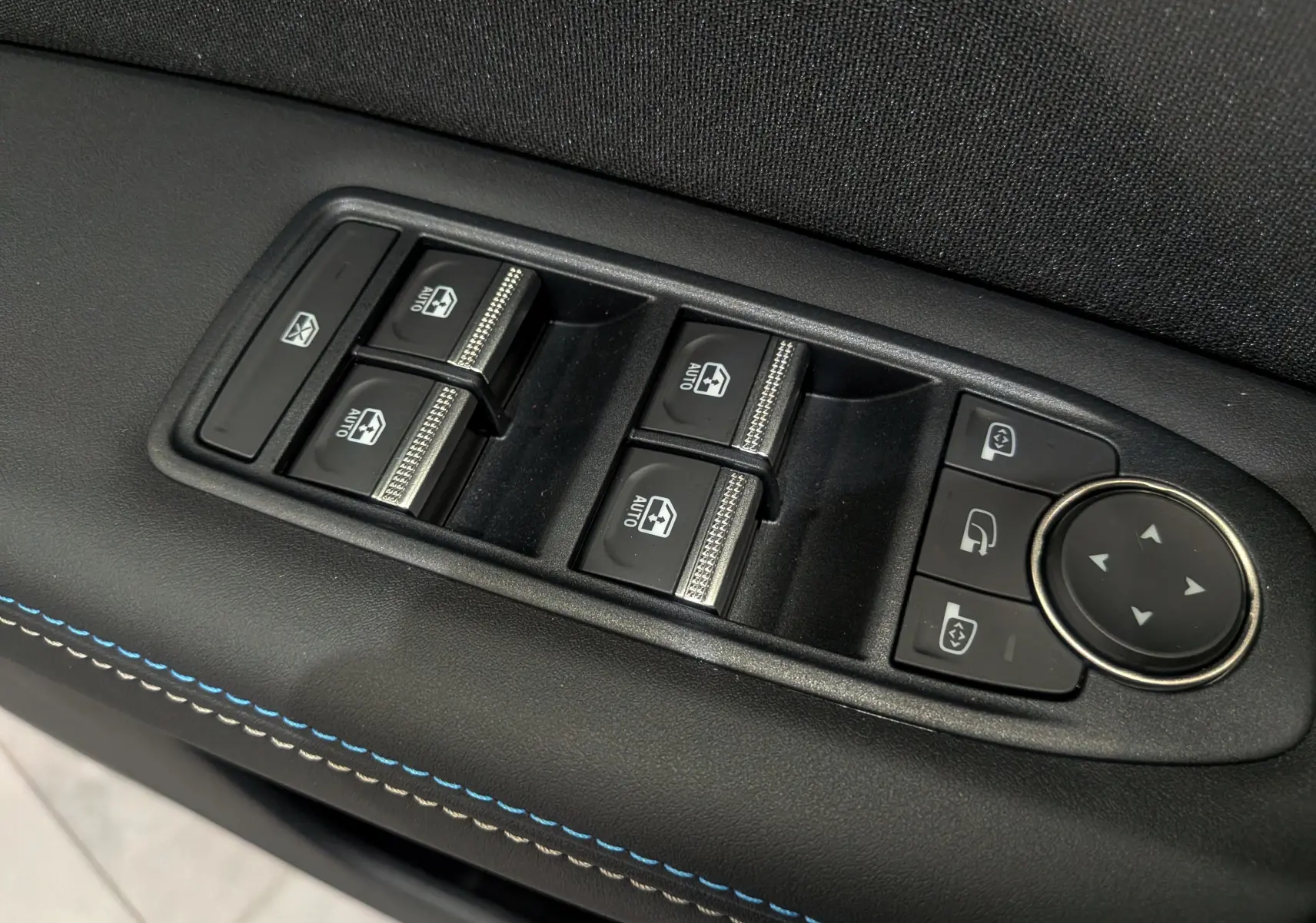 Gros plan sur les commandes des vitres et rétroviseurs côté conducteur du Renault Symbioz gris Rafale avec surpiqûres bleues.