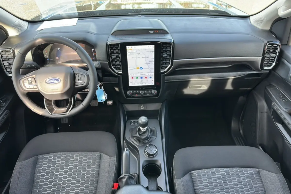 Vue intérieure avant du Ford Ranger 2025 avec tableau de bord noir, volant cuir multifonctions et écran tactile vertical.