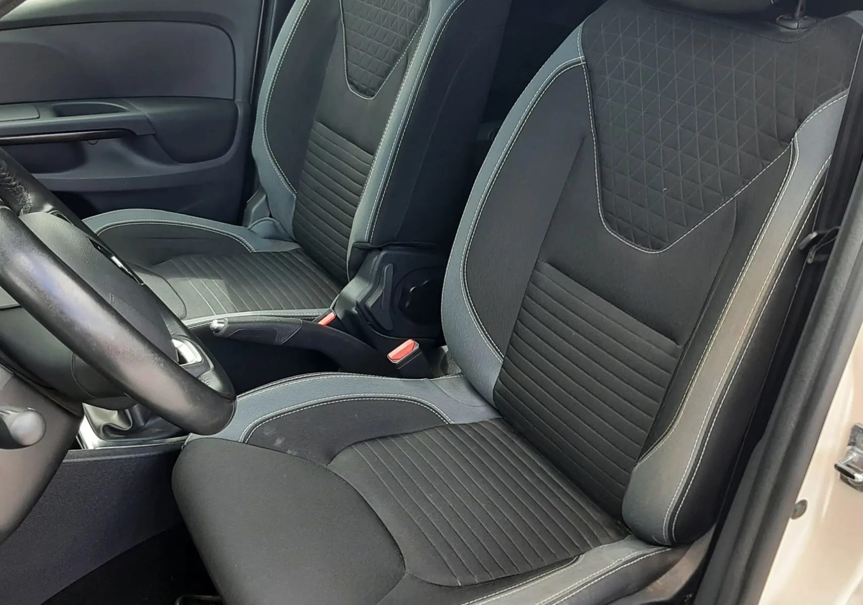 Vue intérieure côté conducteur montrant les sièges en tissu noir avec surpiqûres grises d'une Renault Clio IV Estate beige.