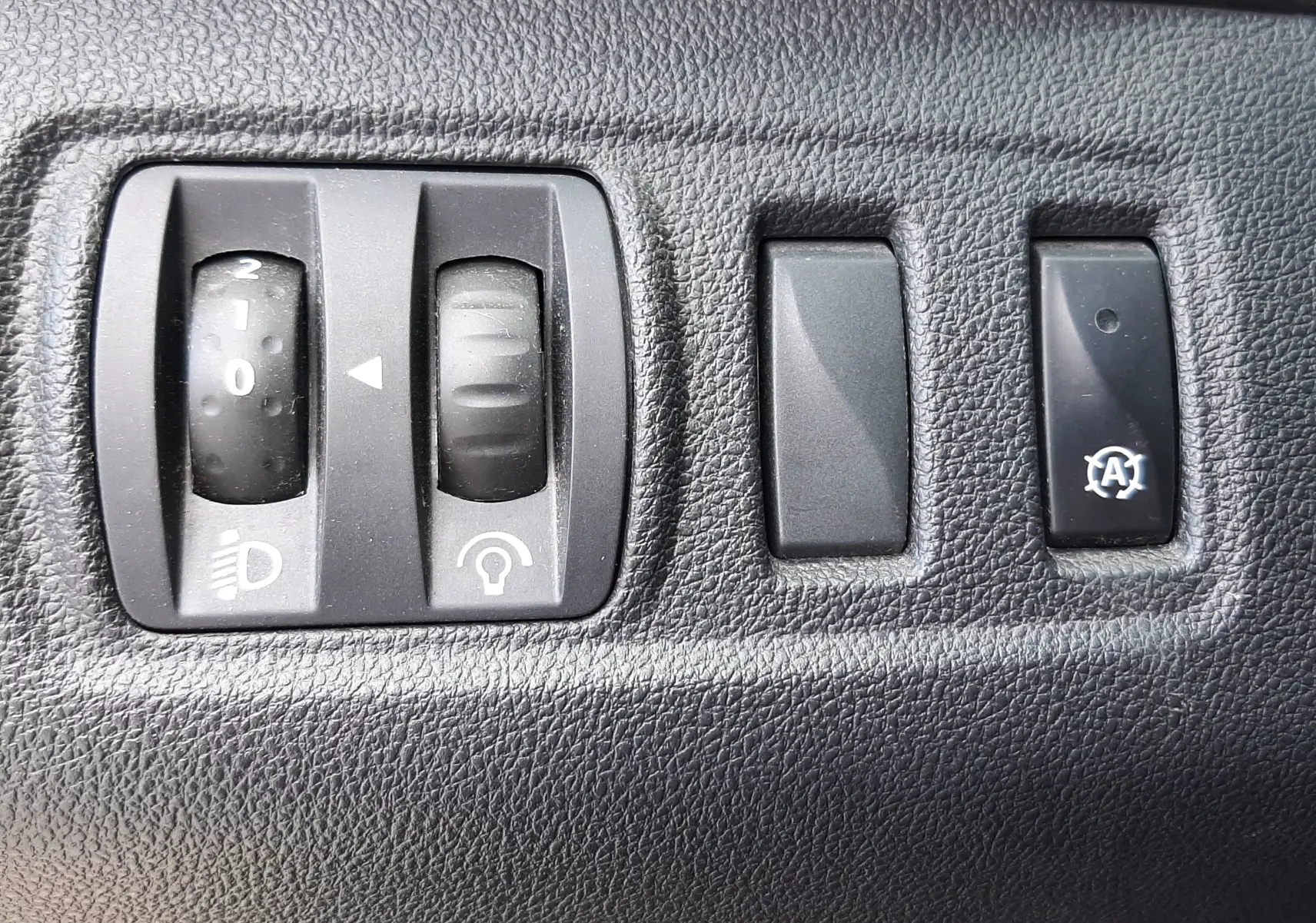 Gros plan sur les commandes noires du tableau de bord de la Renault Clio IV Estate beige, avec réglages d'éclairage et bouton auto-stop.