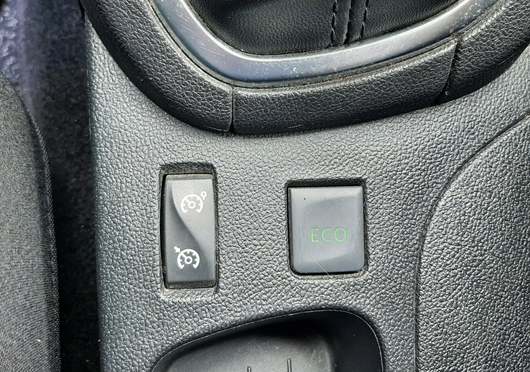 Gros plan sur les commandes du mode ECO et régulateur de vitesse près du levier de vitesses d’une Renault Clio IV beige.