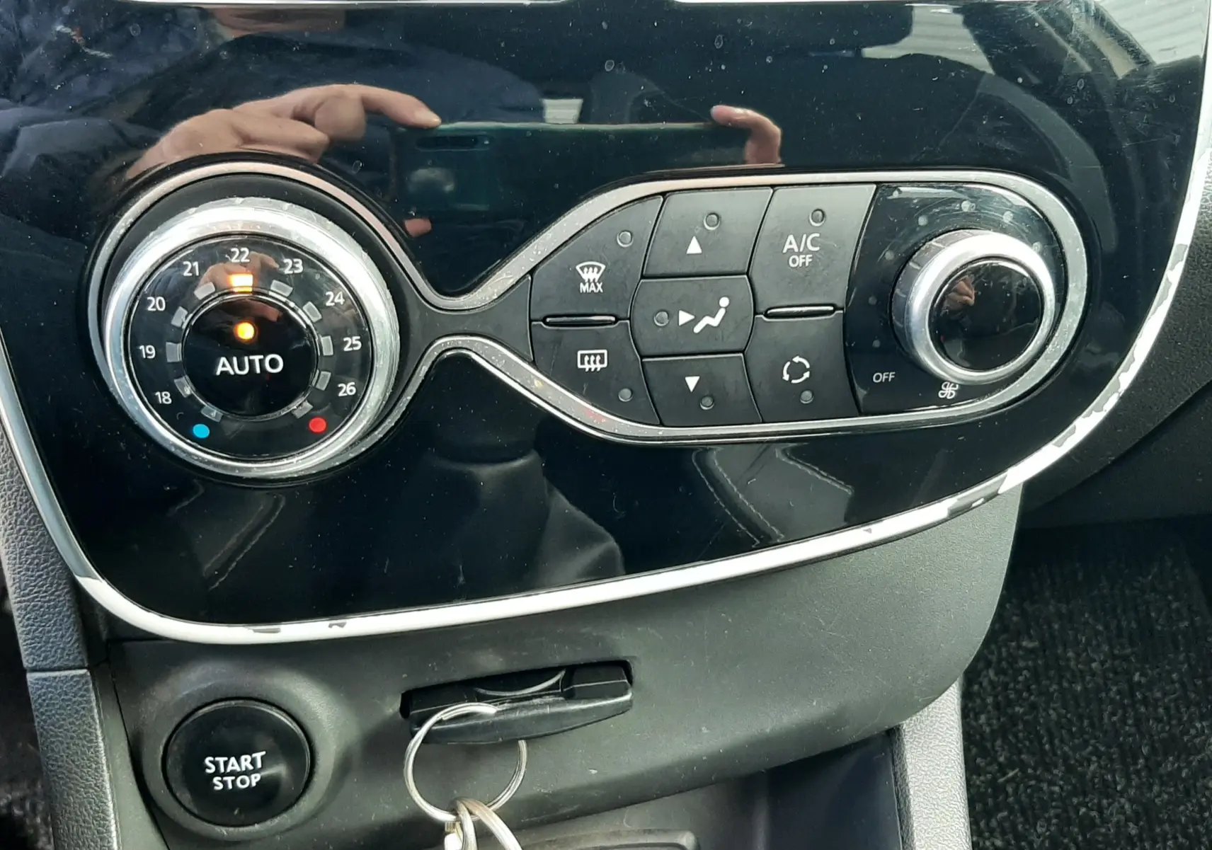 Vue rapprochée du tableau de bord noir de la Renault Clio IV beige, montrant les commandes de climatisation et le bouton start/stop.