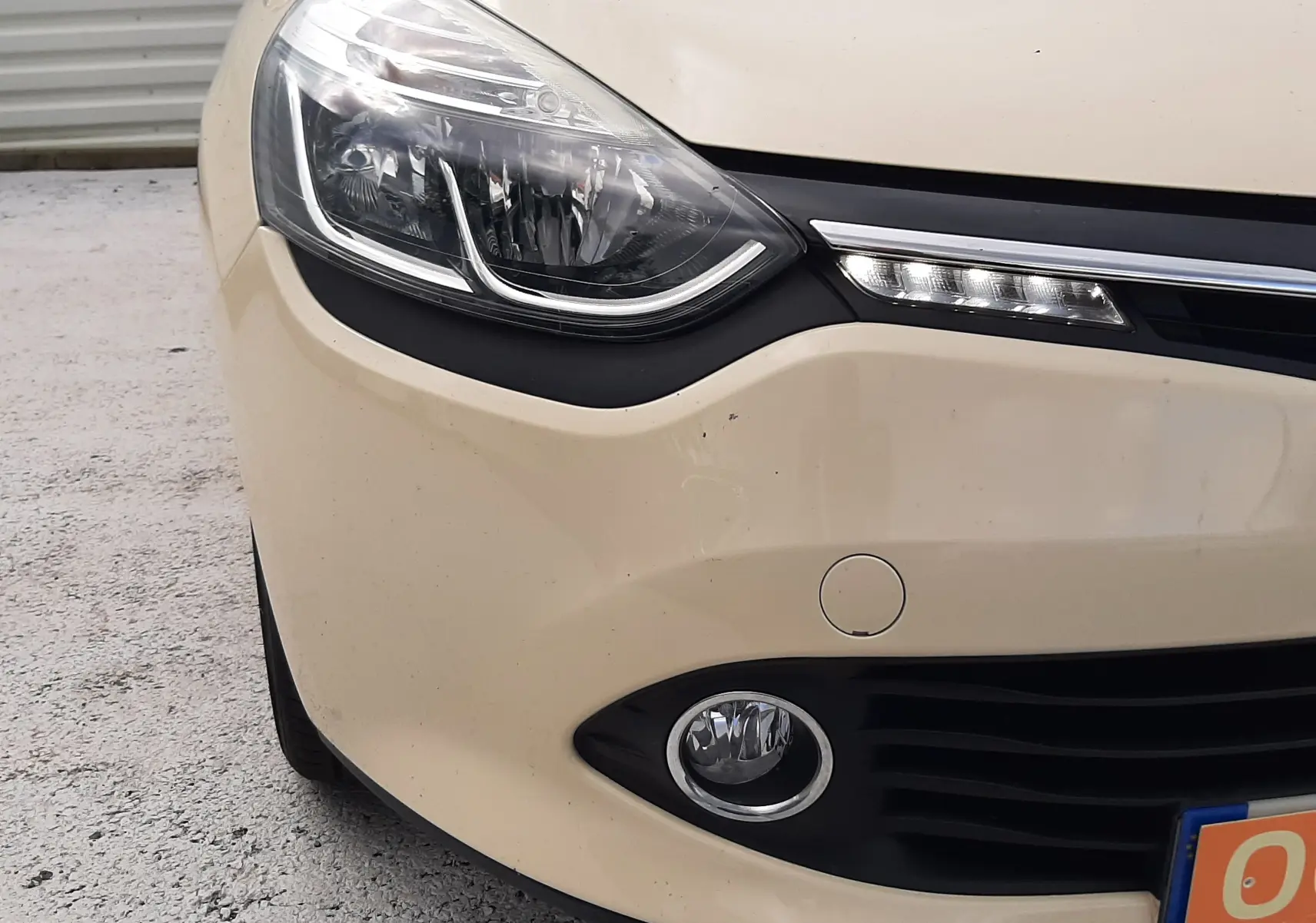 Gros plan sur l'avant gauche beige d'une Renault Clio IV Estate avec phares LED et antibrouillard visibles.