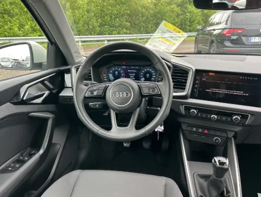 Vue intérieure de face du poste de conduite gris d’un Audi A1 Sportback 2025 avec volant cuir, cockpit numérique et boîte manuelle.