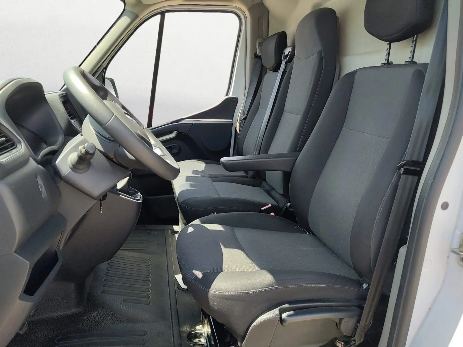 Intérieur du Renault Master blanc 2022 vu de côté gauche, montrant les trois sièges avant en tissu noir et le volant.
