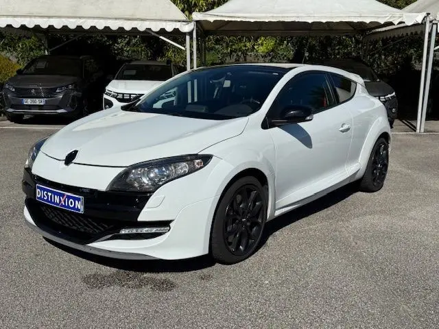 Renault Mégane III Coupé 2.0T RS blanc nacré en 3/4 avant droit avec jantes noires et phares Xenon visibles.