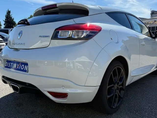 Vue 3/4 arrière droite d'une Renault Mégane III Coupé 2.0T RS blanc nacré avec jantes noires et feux LED distinctifs.