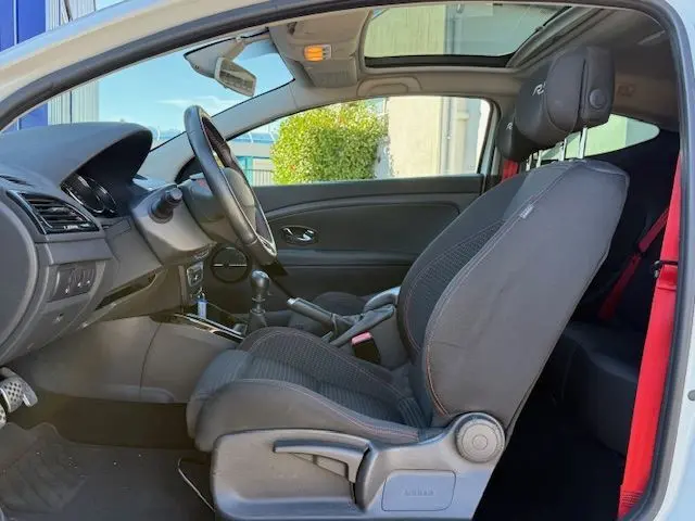 Intérieur côté conducteur de la Renault Mégane III Coupé 2.0T 265cv RS blanc nacré, sièges tissu sport et toit ouvrant panoramique.