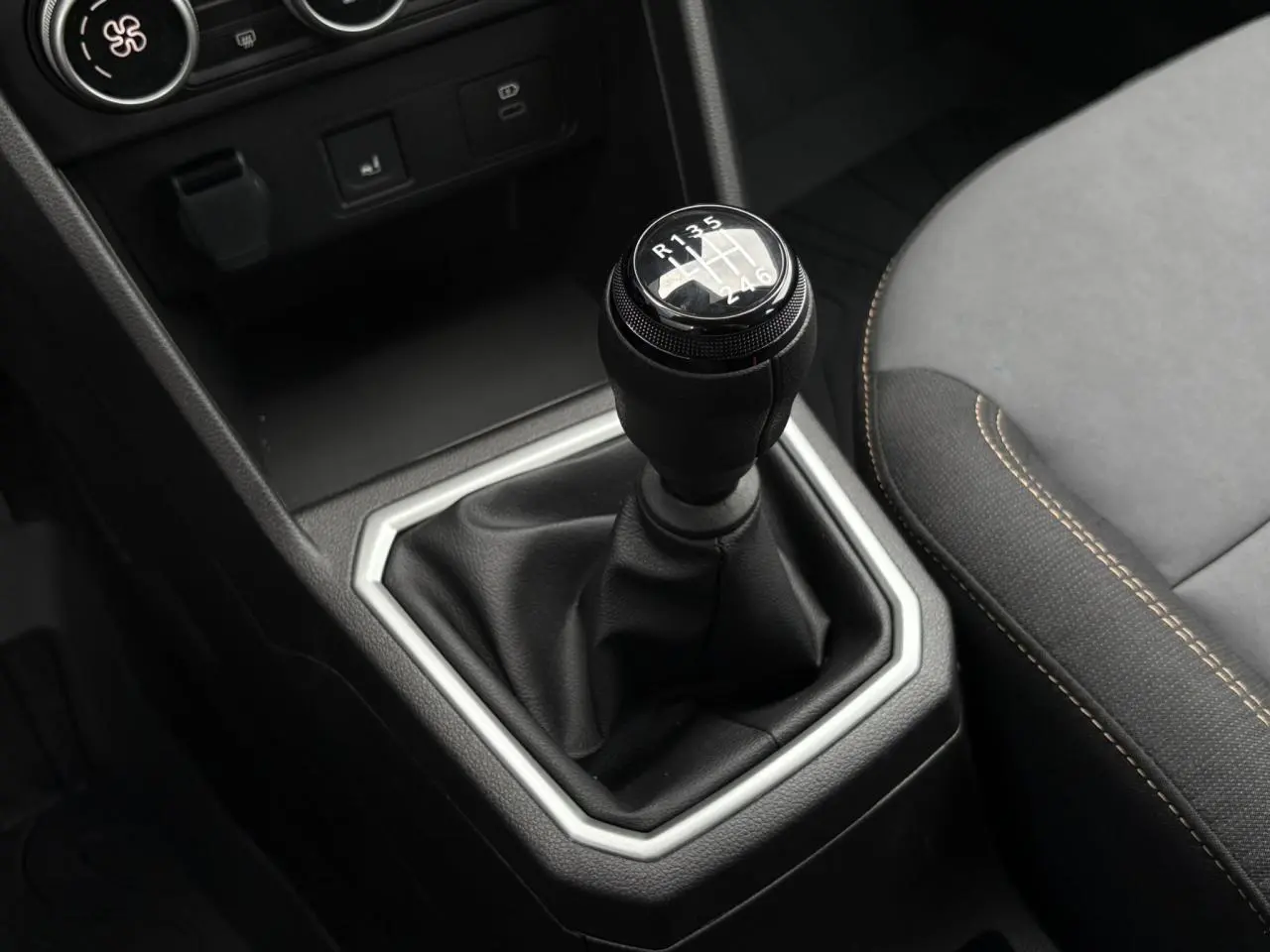 Gros plan sur le levier de vitesses manuel noir entouré d’un cadre argenté, siège avant gris avec surpiqûres beige visible.