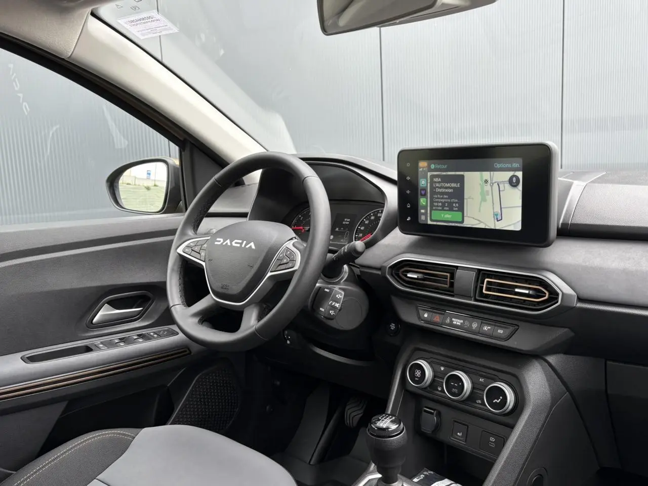 Vue intérieure côté conducteur de la Dacia Sandero Stepway 2025 beige avec volant multifonction et écran tactile GPS.