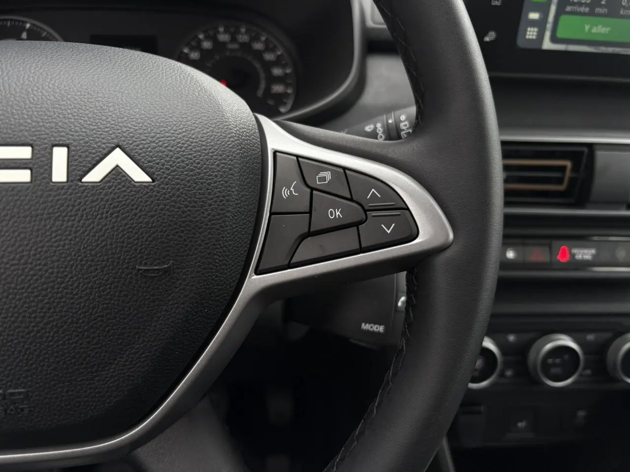 Gros plan sur le volant noir de la Dacia Sandero Stepway 2025, avec commandes multifonctions et tableau de bord en arrière-plan.