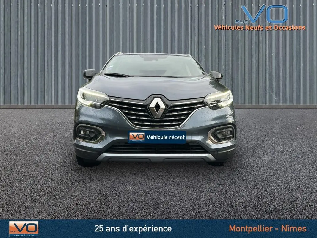 Vue frontale d'un Renault Kadjar gris 2019 avec feux allumés et calandre chromée sur fond industriel.