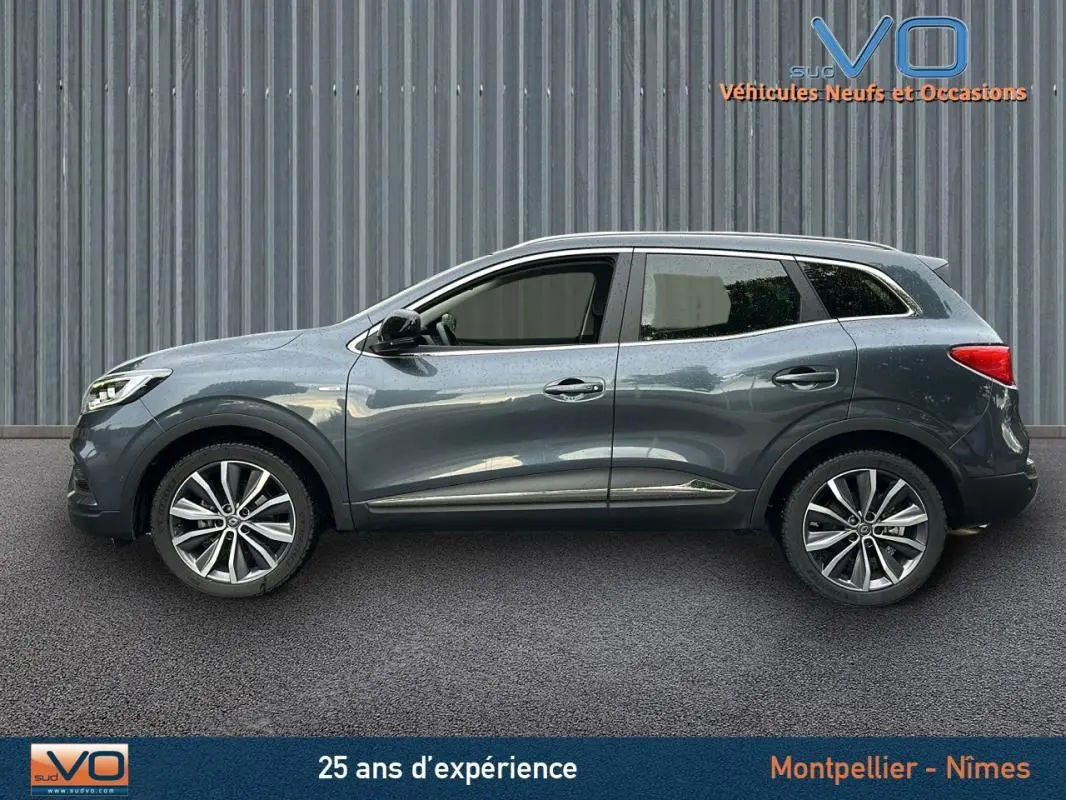 Profil côté gauche du Renault Kadjar gris 2019 avec jantes alliage 18 pouces et barres de toit visibles.