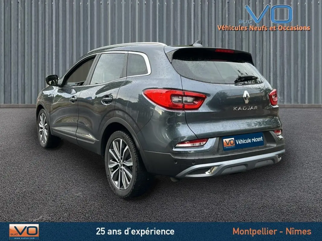 Vue 3/4 arrière droite d'un Renault Kadjar gris 2019 avec jantes alliage 18 pouces et barres de toit visibles.