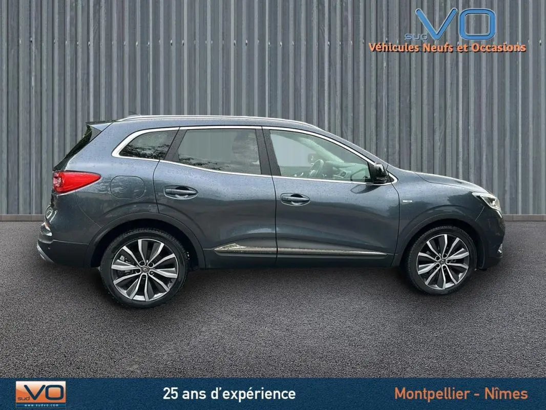 Profil côté droit du Renault Kadjar gris 2019 avec jantes alliage 18 pouces et barres de toit visibles.