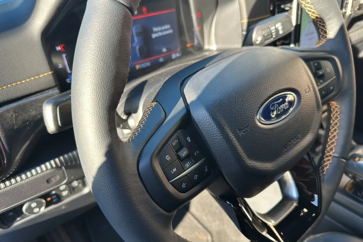 Gros plan sur le volant cuir noir avec surpiqûres orange du Ford Ranger 2025, mettant en valeur les commandes multifonctions.