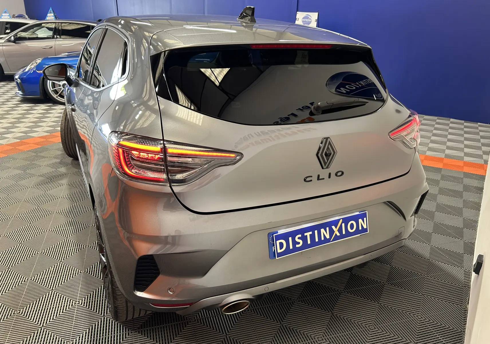 Vue 3/4 arrière droite d'une Renault Clio V gris schiste avec feux arrière allumés dans un showroom.