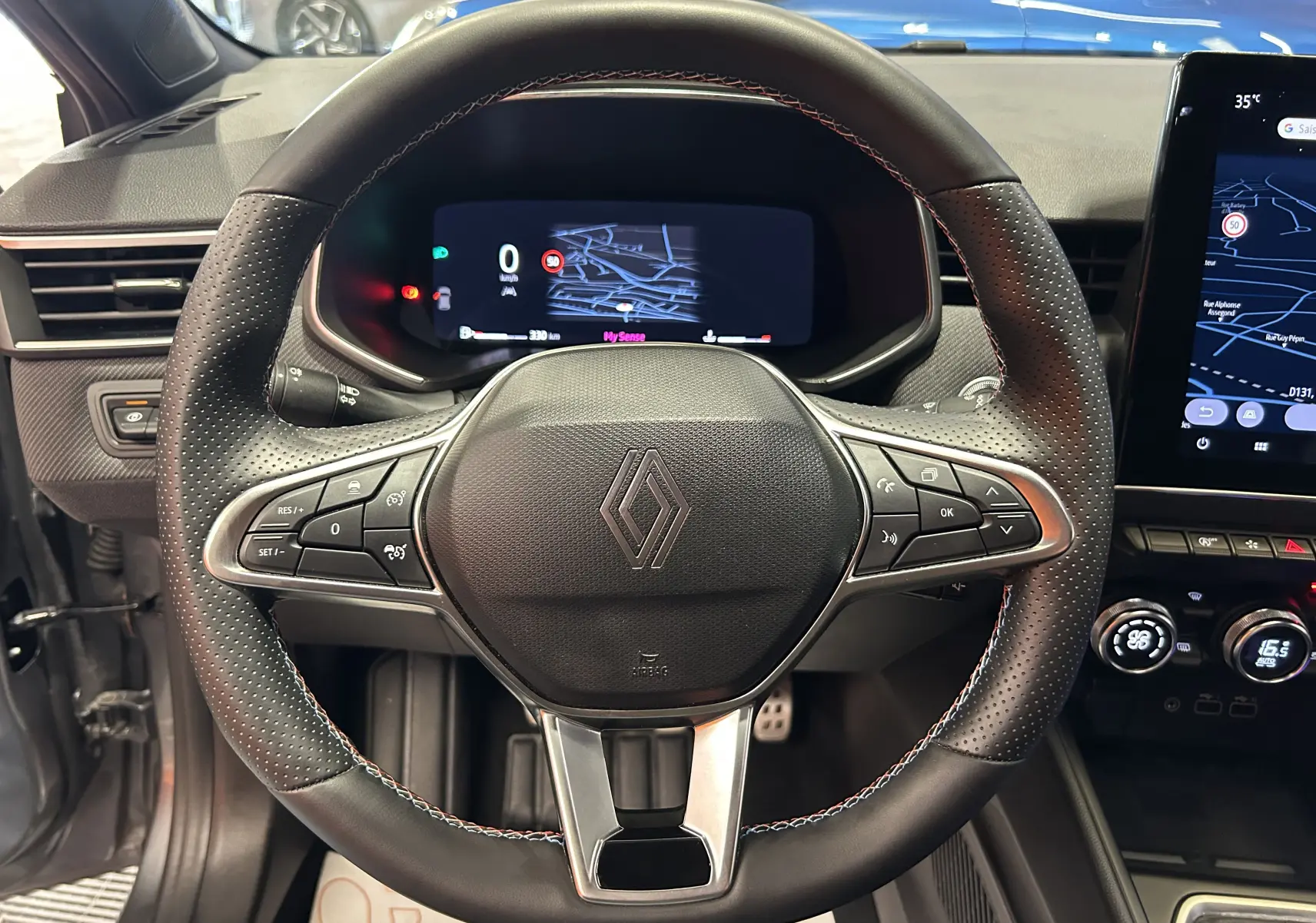 Vue intérieure centrée sur le volant noir perforé de la Renault Clio V TCe 90 Esprit Alpine avec tableau de bord digital.