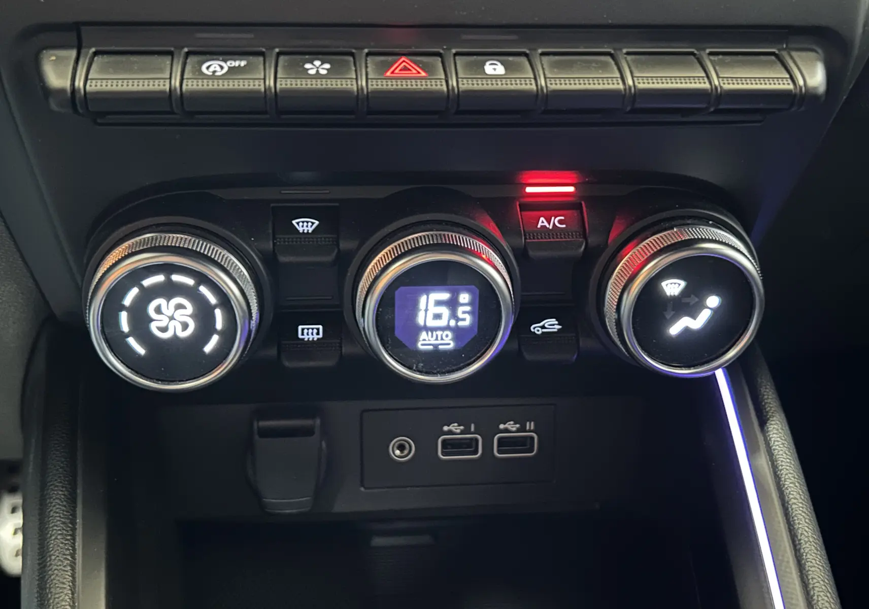 Vue rapprochée de la console centrale de la Renault Clio V gris schiste, avec commandes climatisation et ports USB visibles.