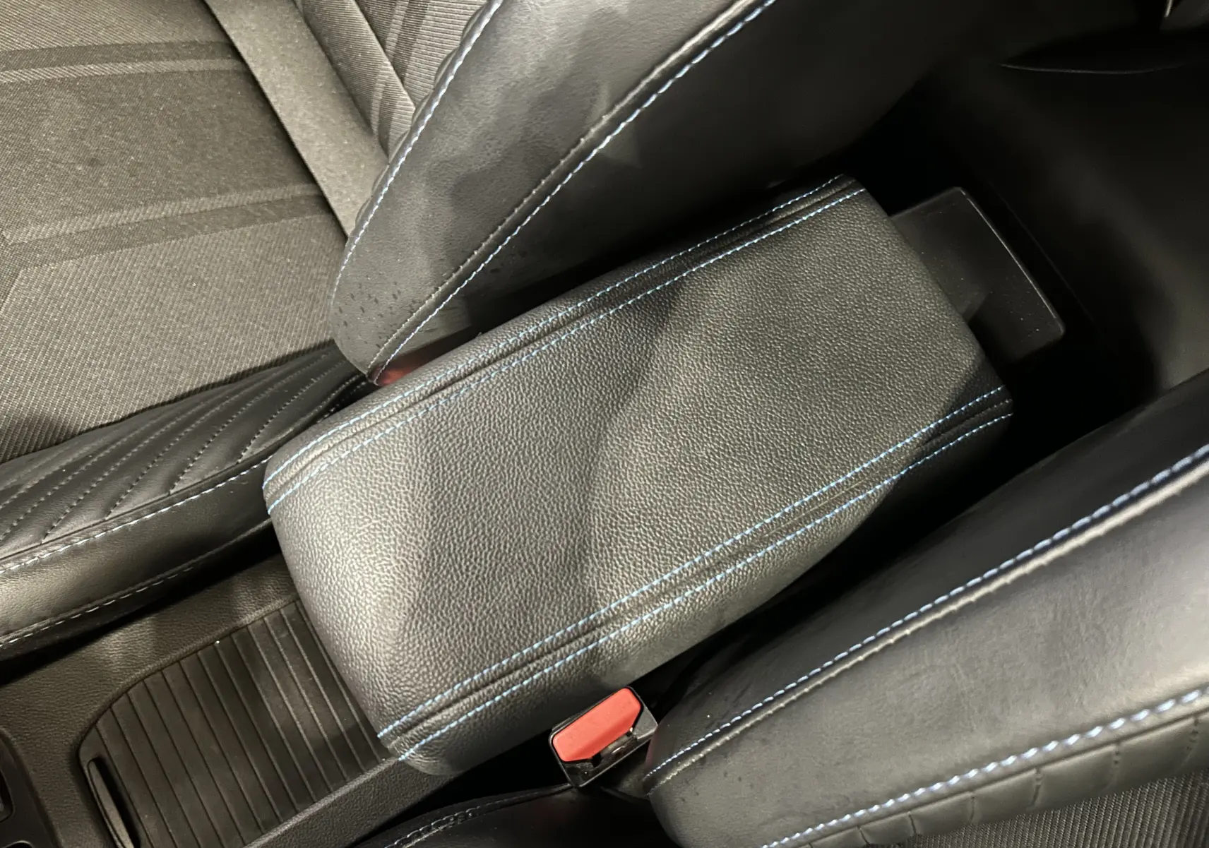 Gros plan sur l'accoudoir central en cuir gris avec surpiqûres bleues, entouré des sièges avant tissu et cuir de la Renault Clio V.