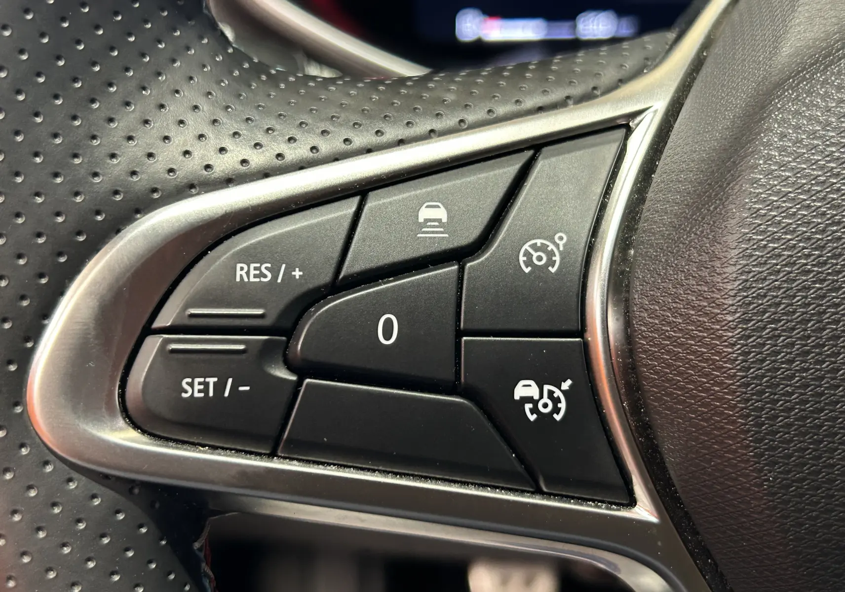 Gros plan sur les commandes de régulateur de vitesse au volant perforé d'une Renault Clio V gris schiste.