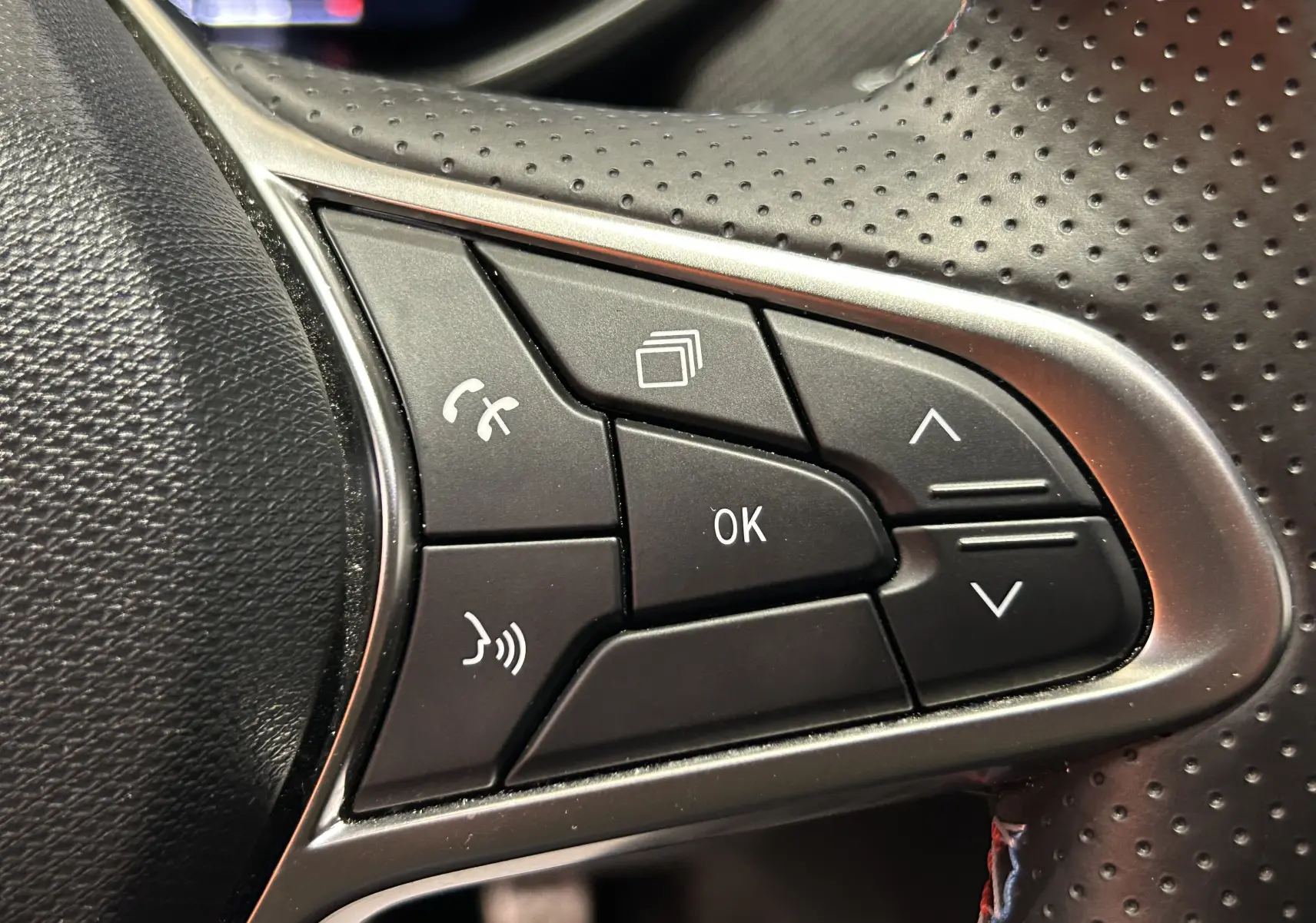 Gros plan sur les commandes multifonctions noires du volant perforé de la Renault Clio V TCe 90 Esprit Alpine gris schiste.