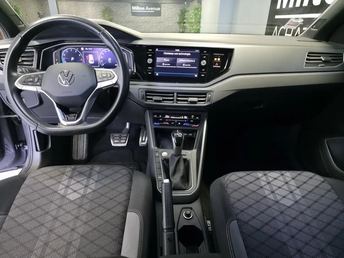 Vue intérieure avant du Volkswagen Taigo 1.5 TSI R-Line, volant cuir multifonctions, tableau de bord digital et sièges tissu noirs à motifs.