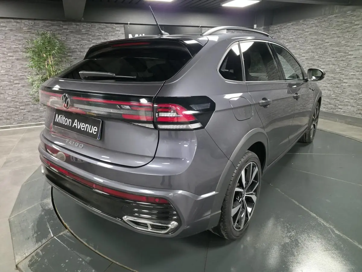 Volkswagen Taigo gris foncé en 3/4 arrière droit, avec jantes noires brillantes et feux arrière LED distinctifs.