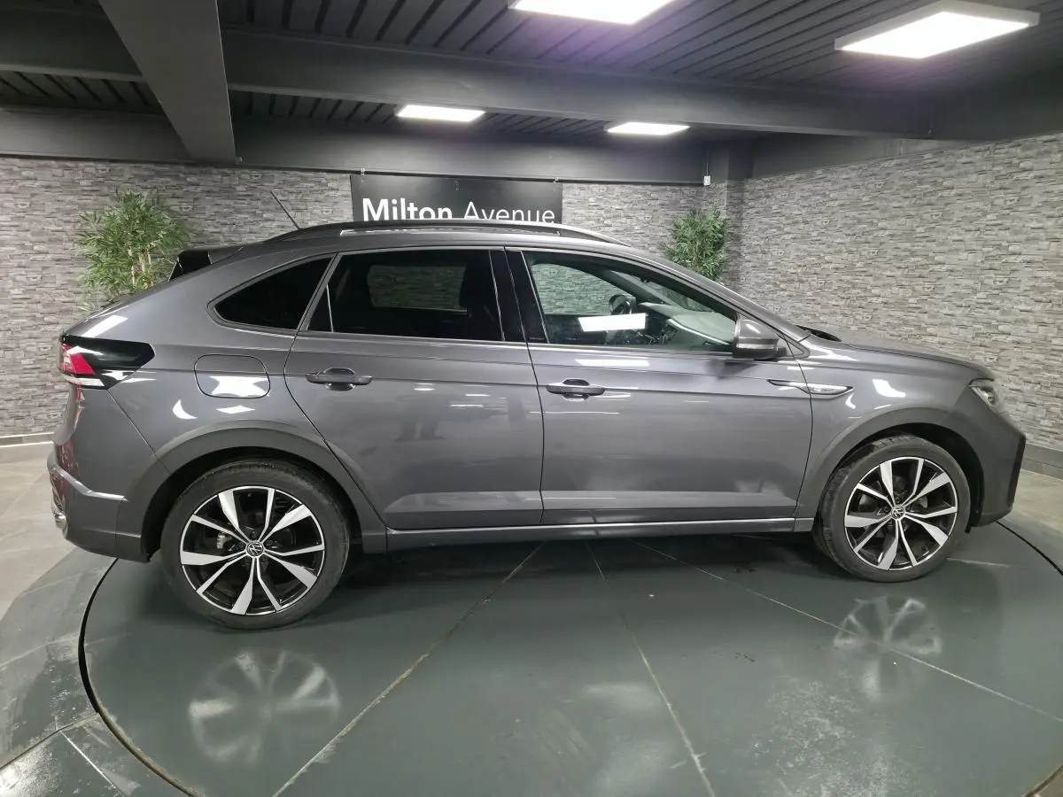 Volkswagen Taigo gris foncé en profil droit, avec jantes alliage noires brillantes et toit noir en intérieur showroom.