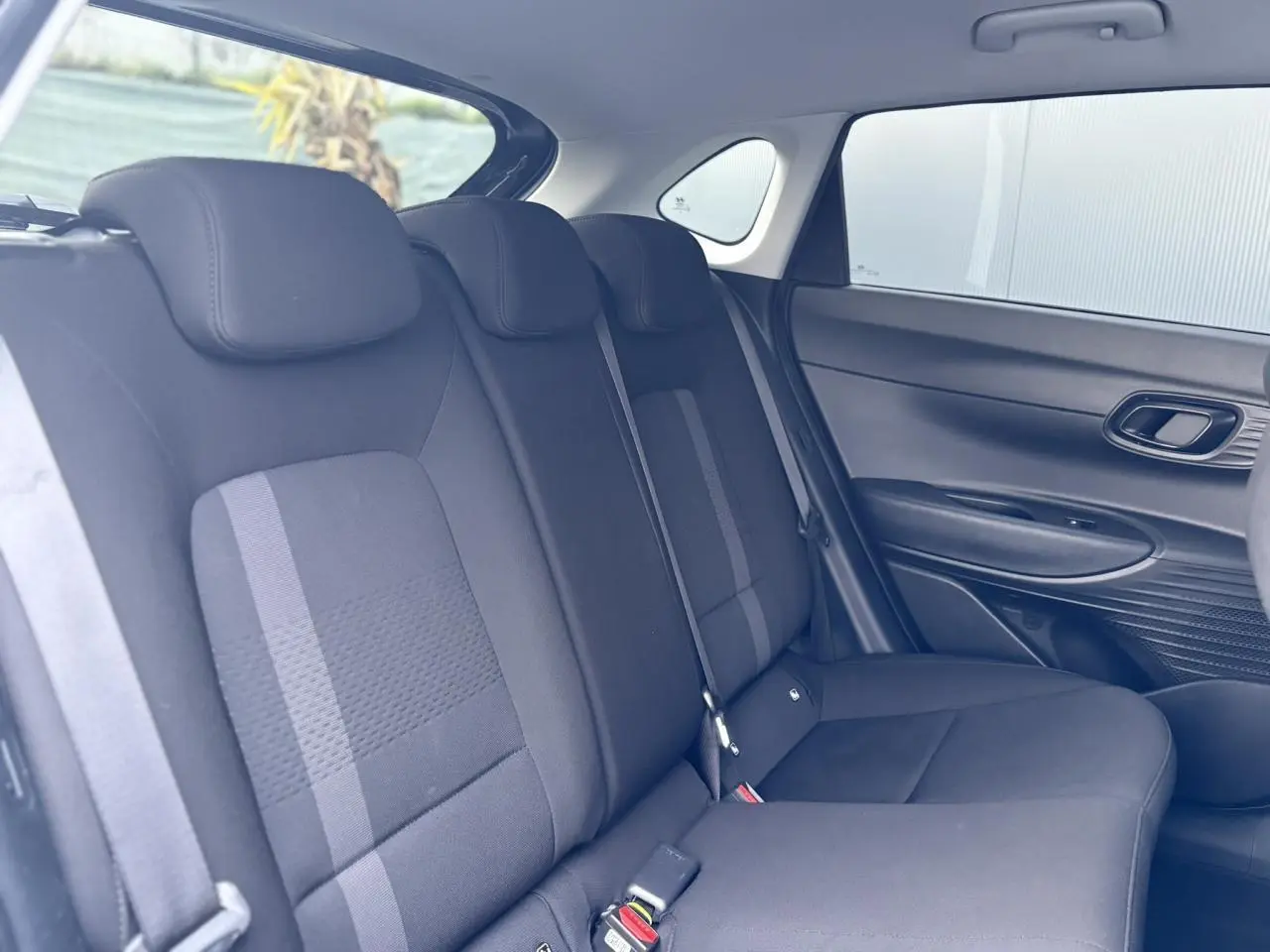 Vue intérieure côté droit des sièges arrière noirs de la Hyundai i20 2025 avec ceinture et garnitures de porte visibles.