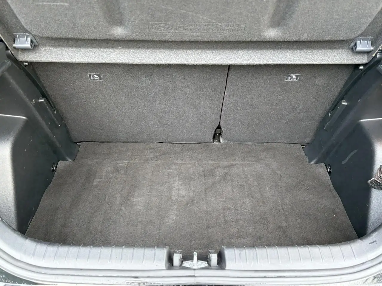 Vue du coffre ouvert d'une Hyundai i20 2025 noir Phantom Metal, montrant l'espace de chargement vide et la moquette intérieure.