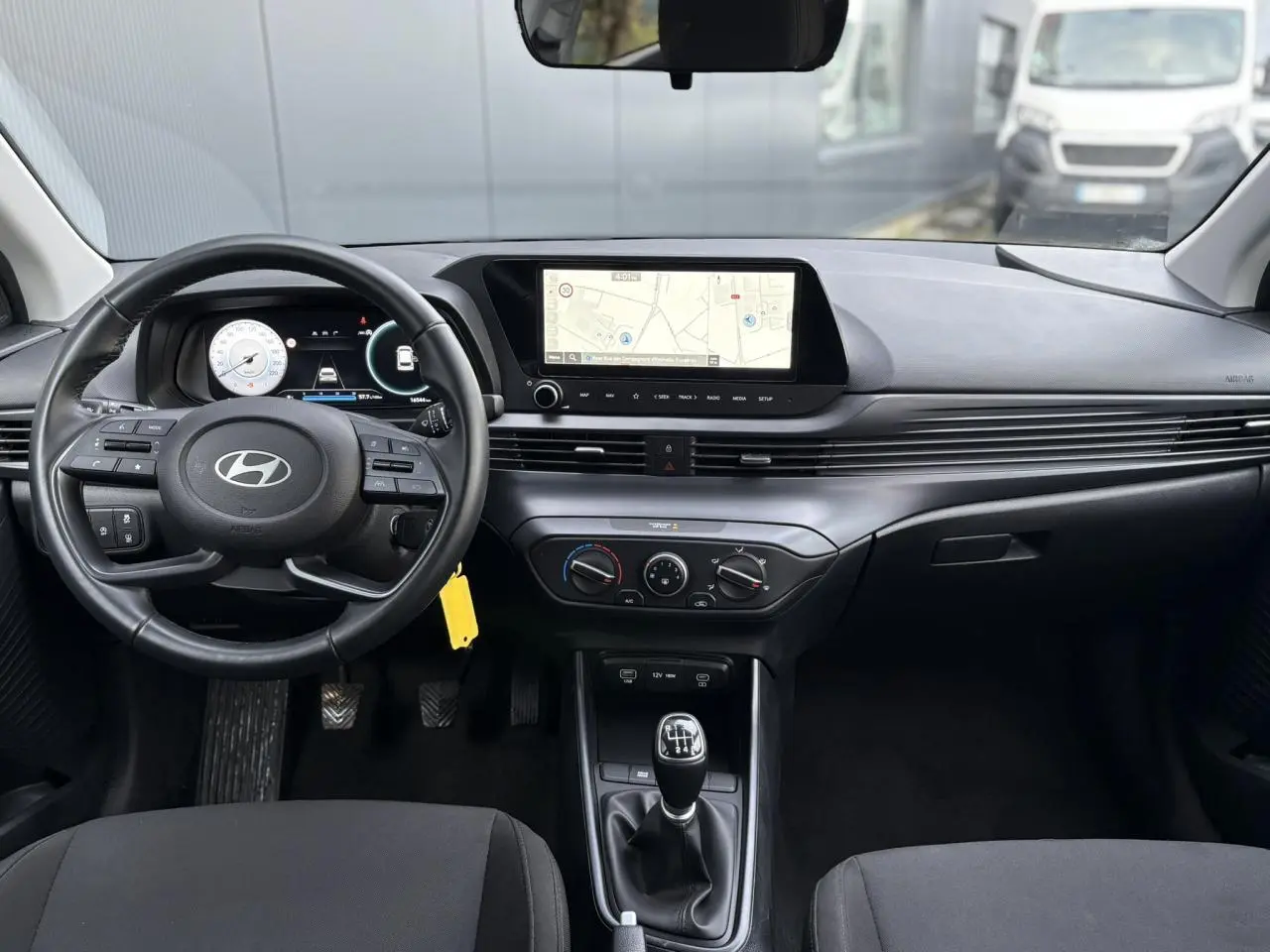Vue intérieure avant de la Hyundai i20 2025 avec tableau de bord moderne, écran tactile GPS et volant cuir noir.