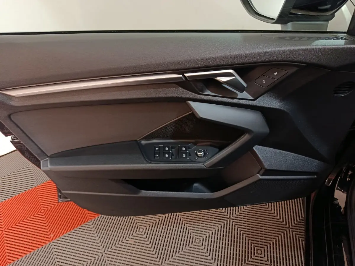 Vue intérieure côté gauche de la porte noire d’une Audi A3 35 TDI 150 S tronic Business Line avec commandes de vitres et rétroviseurs.