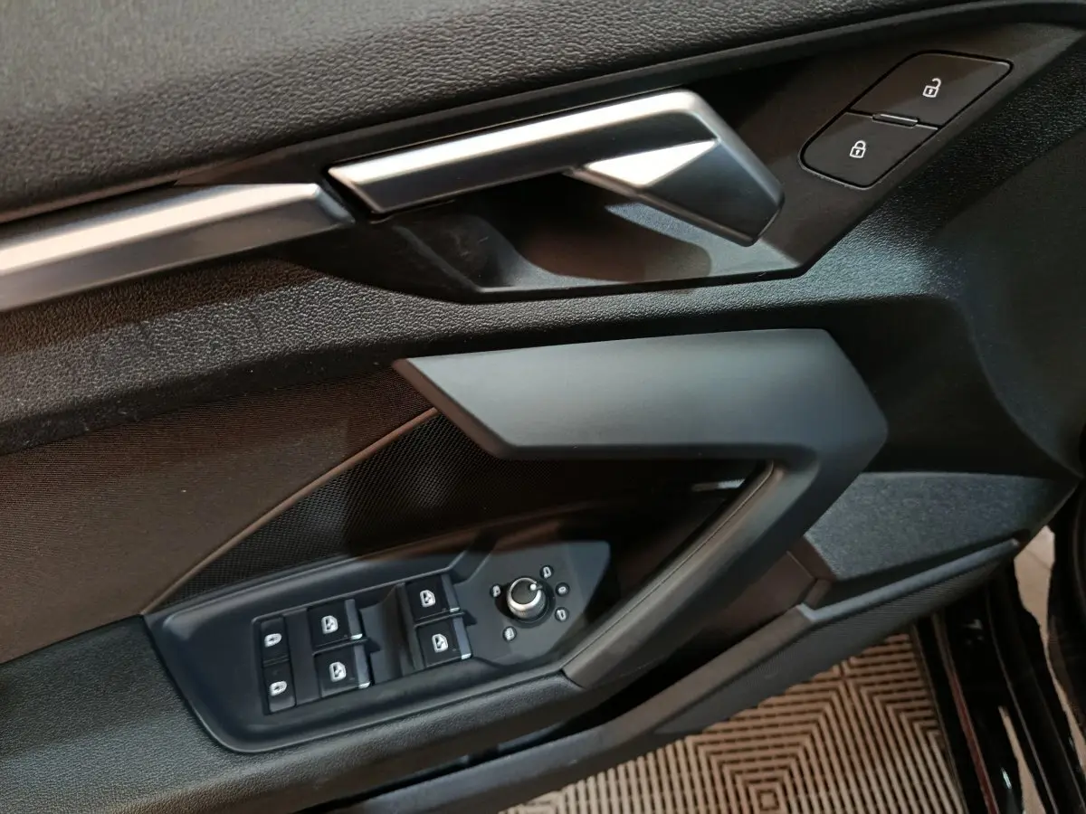 Gros plan sur la porte avant gauche noire de l'Audi A3 35 TDI 2023 avec commandes des vitres et serrure.