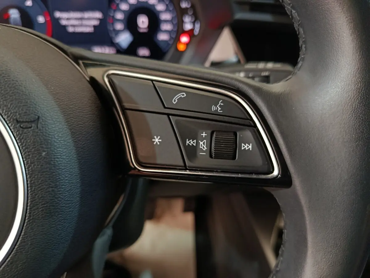 Gros plan sur les commandes vocales et audio au volant cuir de l'Audi A3 35 TDI noir, tableau de bord numérique en arrière-plan.