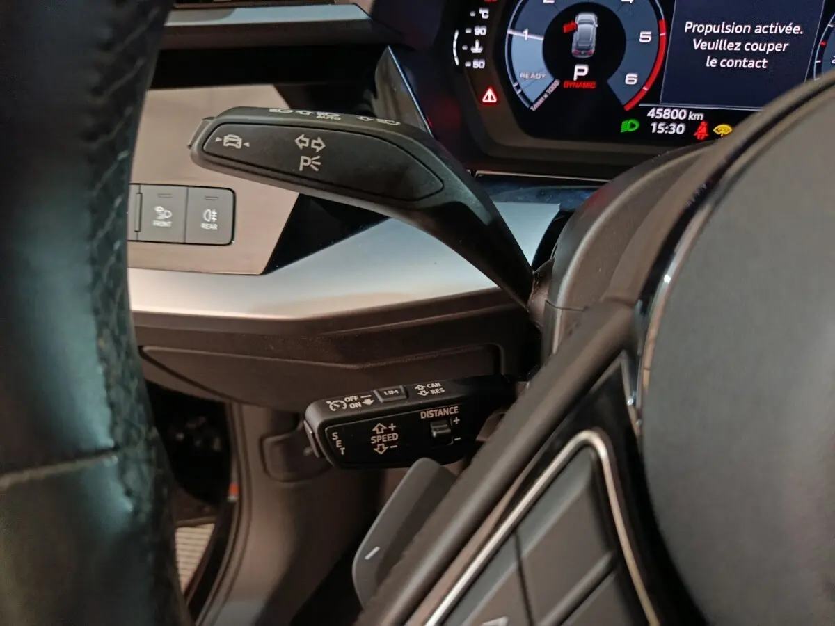 Gros plan sur le volant cuir et les commandes au volant côté gauche de l’Audi A3 35 TDI noire avec tableau de bord digital.