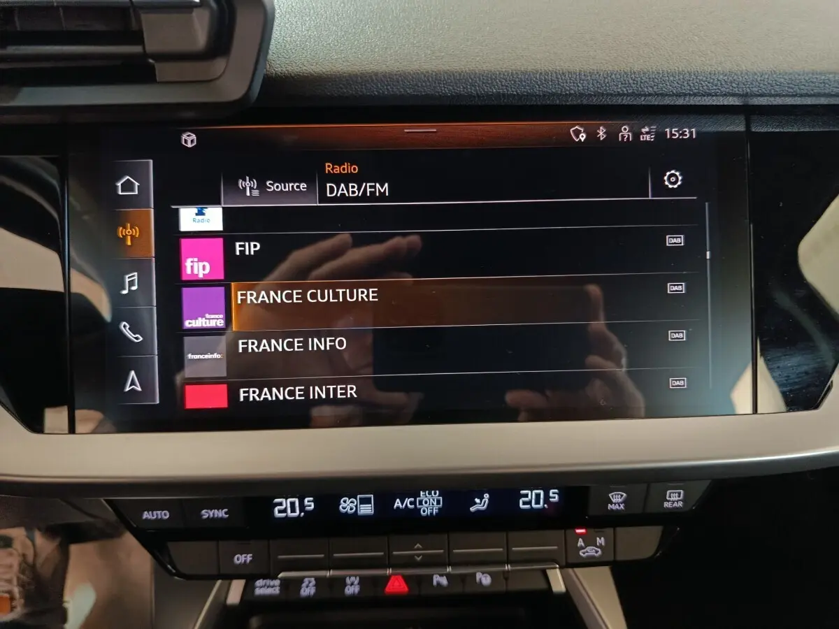 Écran tactile central de l’Audi A3 Business Line 2023 affichant les stations radio DAB/FM, avec commandes climatisation en dessous.