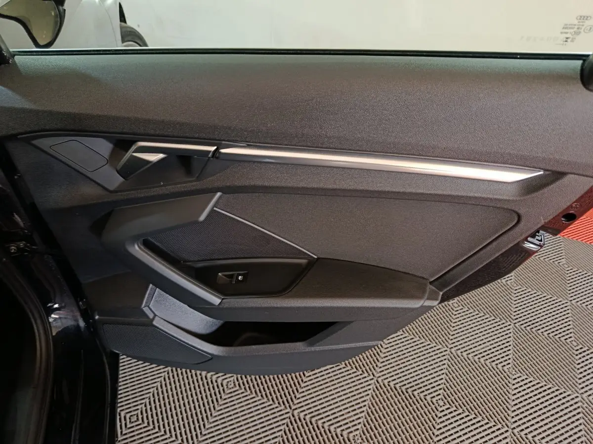 Vue rapprochée de la porte avant gauche noire d’une Audi A3 35 TDI 150 S tronic Business Line avec garniture moderne et poignée argentée.
