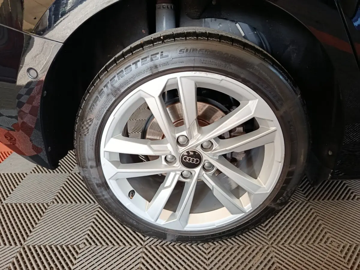 Gros plan sur la roue avant droite d'une Audi A3 noire, jante alliage argentée à cinq doubles branches.